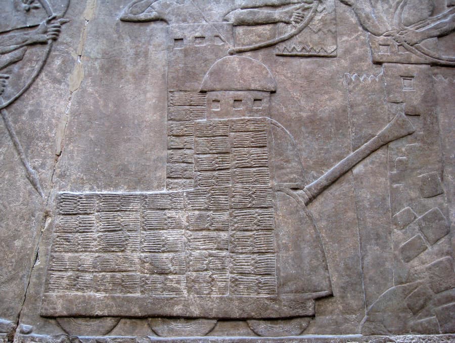 A large, wheeled Assyrian battering ram with an observation turret attacks the collapsing walls of a besieged city. From the North-West Palace at Nimrud, about 865-860 BC.